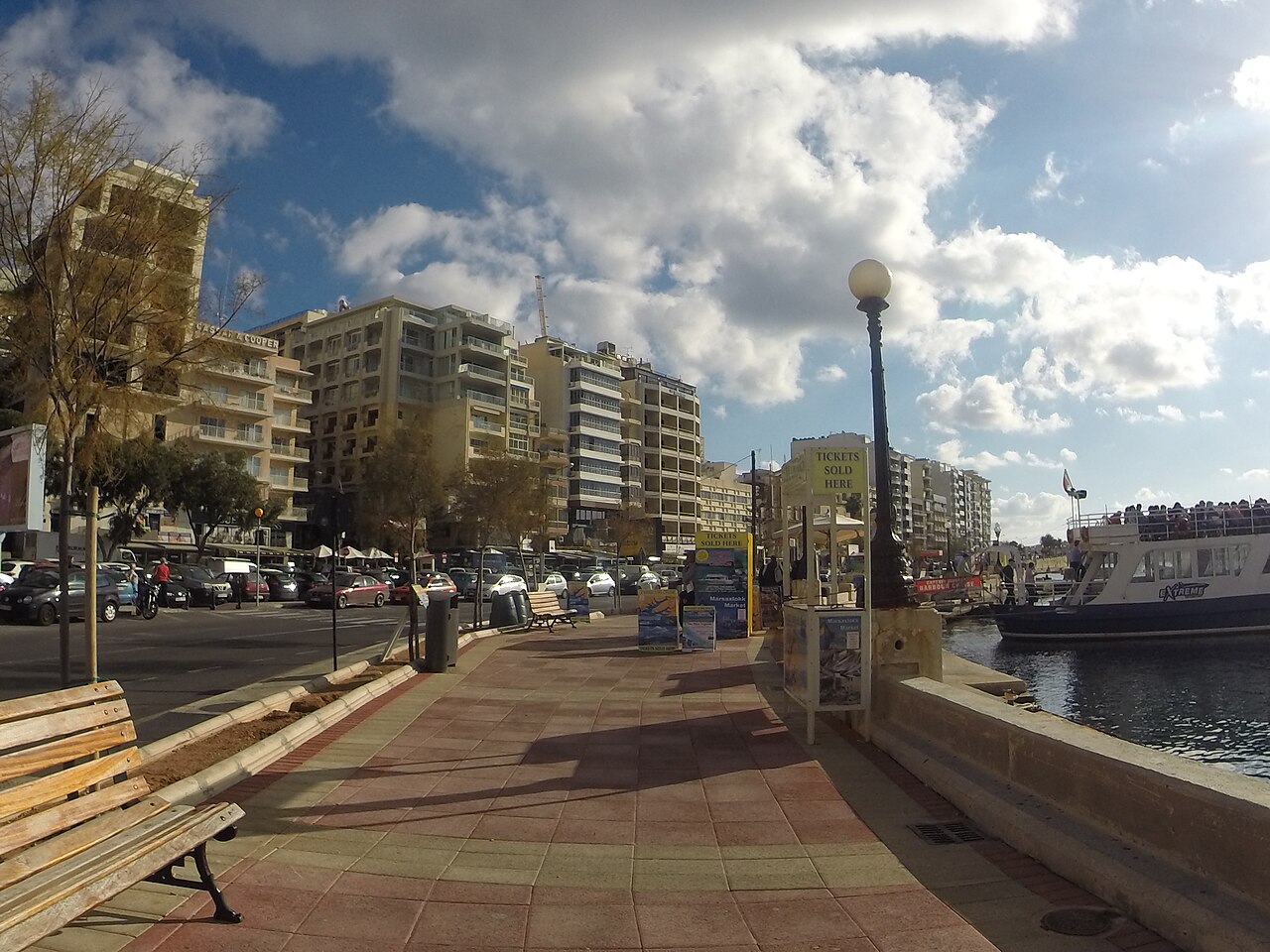 Tree-lined Sliema promenade beside the sea with apartment buildings…