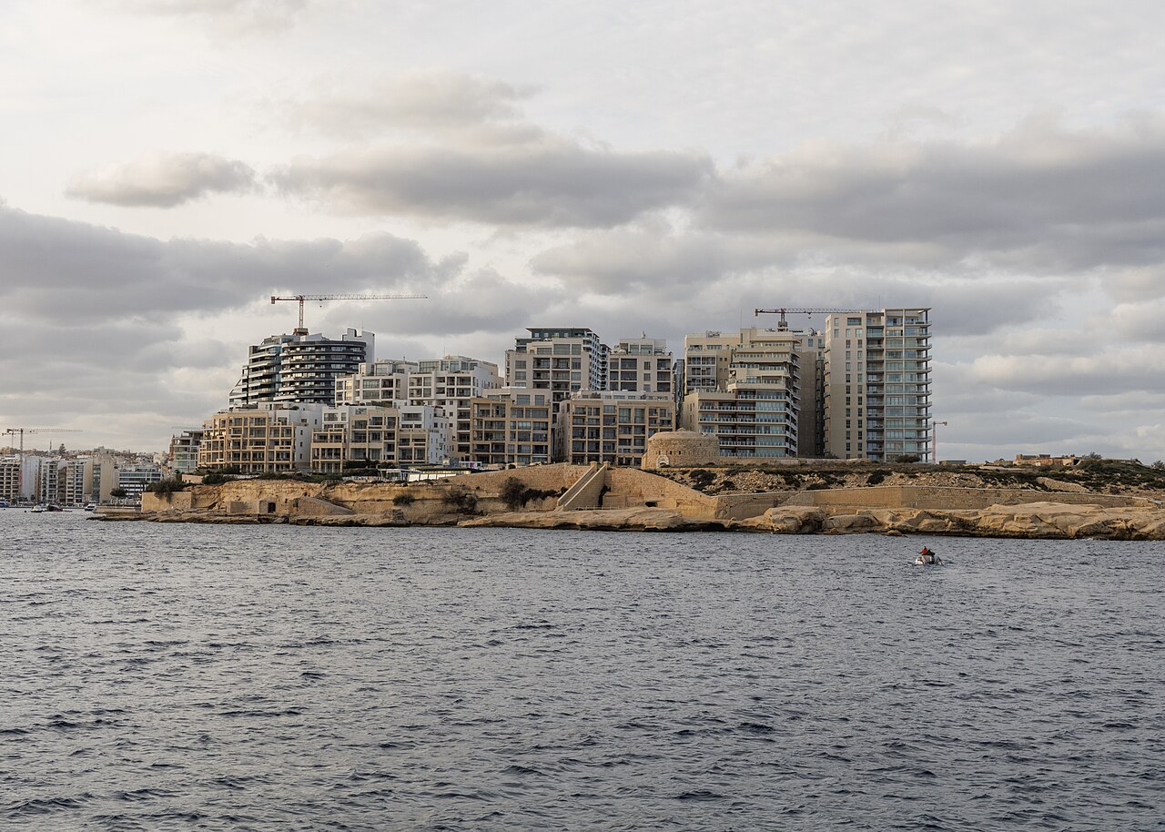 Tigné Point apartment blocks above the rocky shore, seen across the…